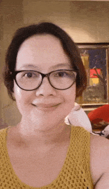 a woman wearing glasses and a yellow tank top is smiling at the camera .