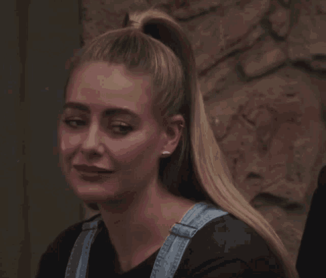 a woman with a ponytail is wearing a black shirt and overalls