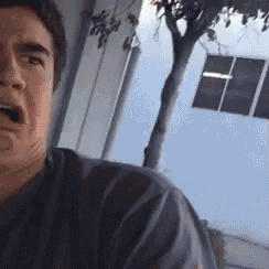 a man is making a funny face in front of a tree and a building .
