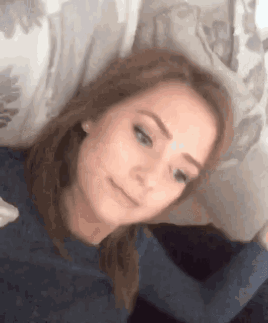 a woman in a blue shirt is laying on a bed with her head on a pillow