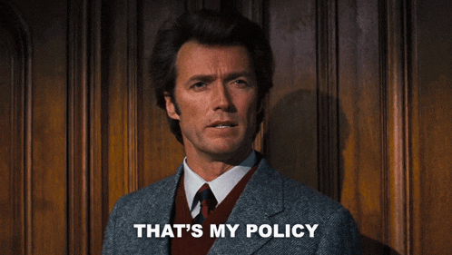a man in a suit says that 's my policy in front of a wooden wall