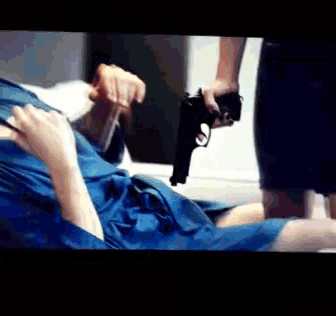 a woman is holding a gun in front of a man in a blue shirt