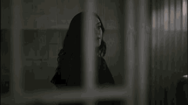 a woman is standing behind bars in a dark room looking at the camera .