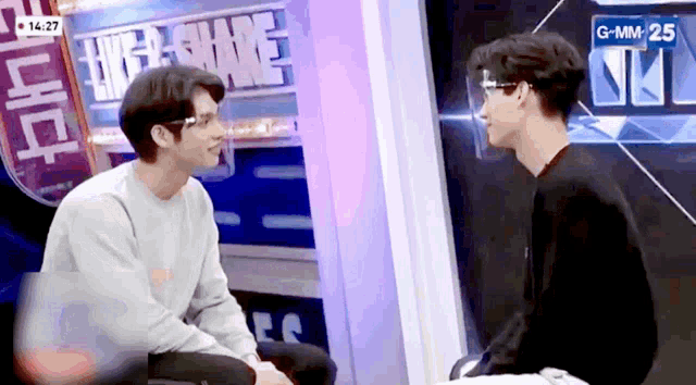 two men wearing face shields are sitting next to each other in front of a sign that says gmm 25