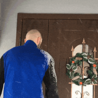 a man in a blue jacket stands in front of a door with a wreath on it