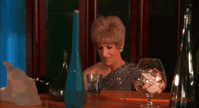 a woman sitting at a table with a glass of water and a bowl of money says hey