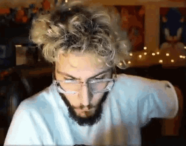 a man with glasses and a beard is sitting in front of a computer screen .
