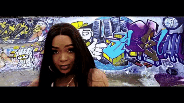 a woman is standing in front of a wall with graffiti on it that says ' a ' on it