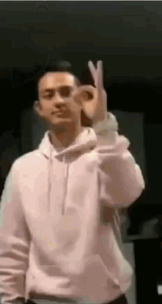 a man in a white hoodie is making an okay sign with his hands .