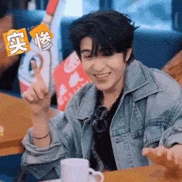 a man in a denim jacket is sitting at a table with a cup of coffee and smiling