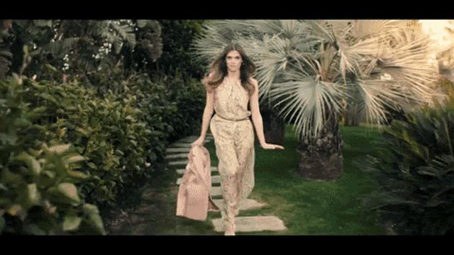a woman in a floral jumpsuit is walking through a garden