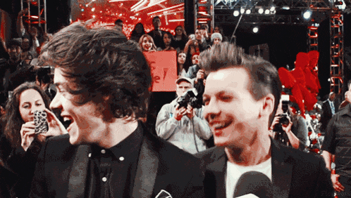 two men are laughing in front of a crowd with a sign that says ' fe ' on it