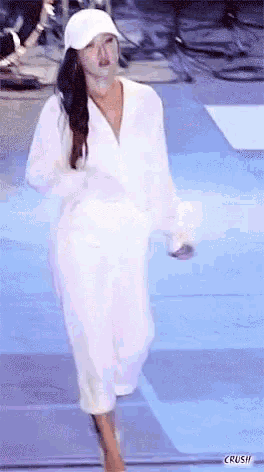 a woman is dancing on a stage wearing a white hat and a white robe .