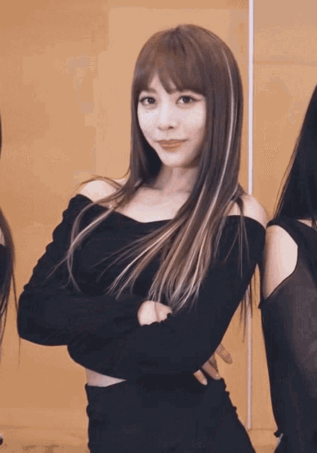 a woman in a black off the shoulder top with her arms crossed looks at the camera