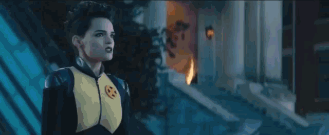 a woman in a fire suit is standing in front of a building with a fire coming out of her chest .
