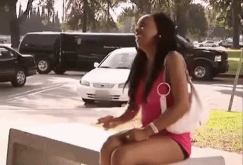 a woman in a pink dress is sitting on a bench in a parking lot with cars parked in the background .