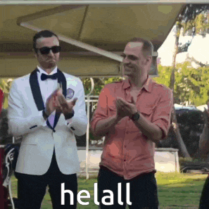 a man in a tuxedo applauds while another man in an orange shirt looks on