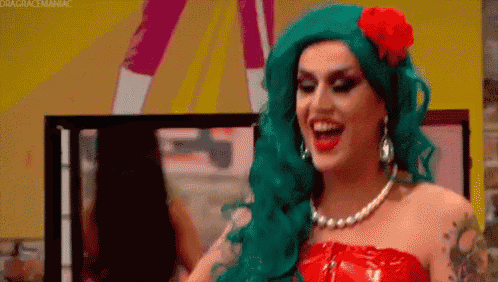 a drag queen with green hair is wearing a red dress and a flower in her hair .