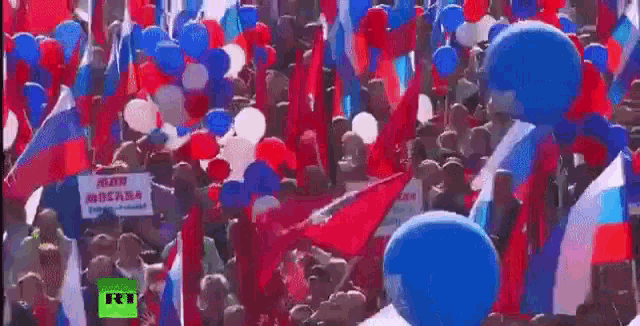 a crowd of people holding russian flags and balloons at a protest .