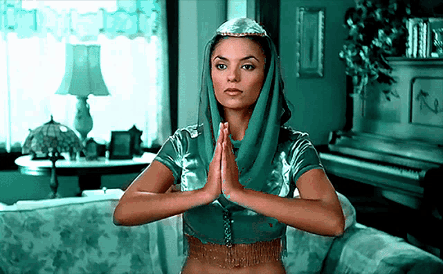 a woman in a green top and head scarf is praying