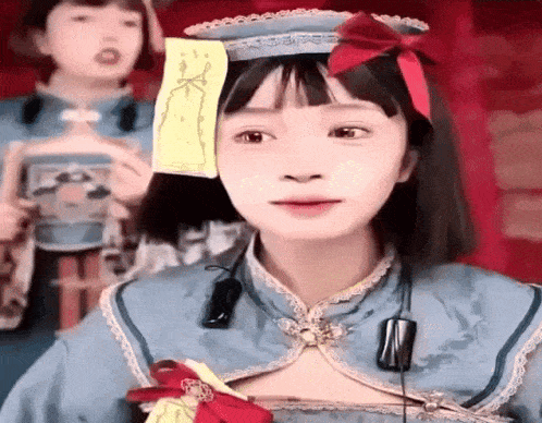 a girl is wearing a blue dress and a hat with a red bow and a sticky note on her head .