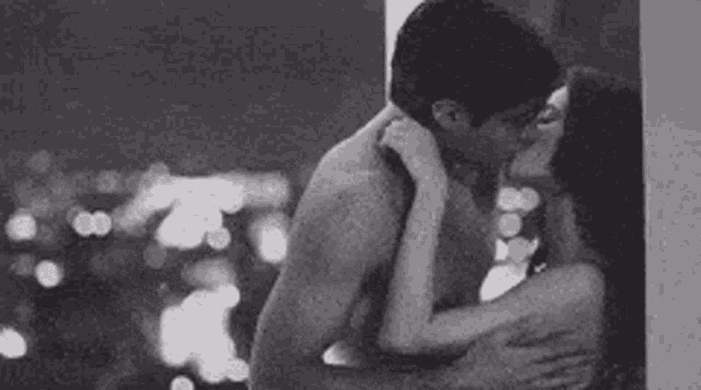 a man and a woman are kissing in front of a window in a black and white photo .