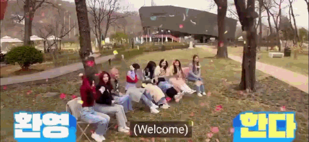 a group of girls are sitting in a park with a welcome sign in the foreground .