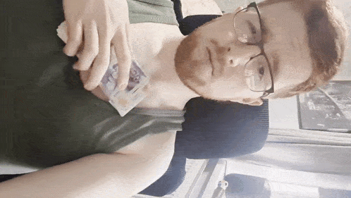 a man wearing glasses and a green tank top is holding a piece of money in his hand ..