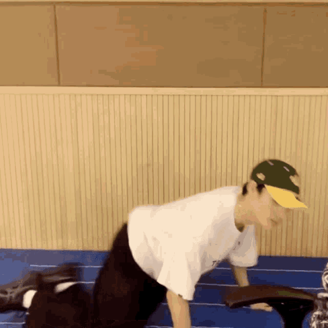 a man in a white shirt and green hat is doing push ups on a blue mat .