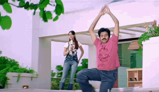 a man in a pink shirt is doing yoga while a woman looks on