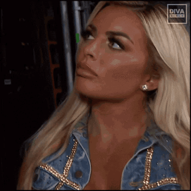 a blonde woman wearing a denim jacket and earrings is looking up at something .