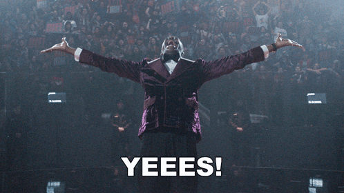 a man in a purple tuxedo is standing in front of a crowd with the words yeees behind him