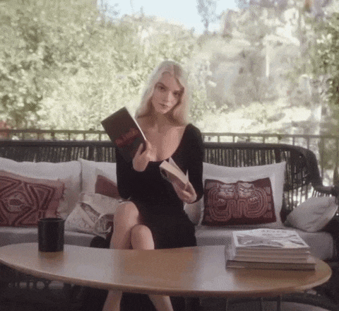a woman in a black dress sits on a couch reading a book called the book