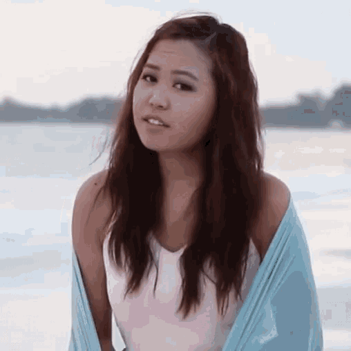 a woman with long hair is standing on a beach with a blue scarf around her shoulders .