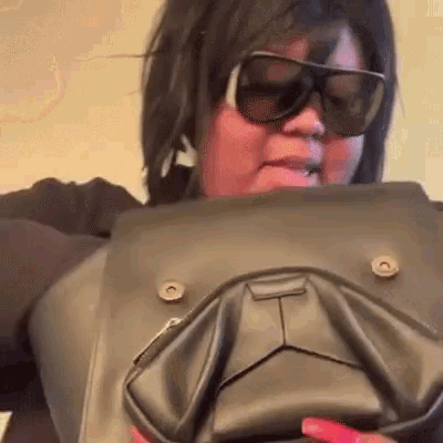a woman wearing sunglasses is holding a black bag that looks like a dog