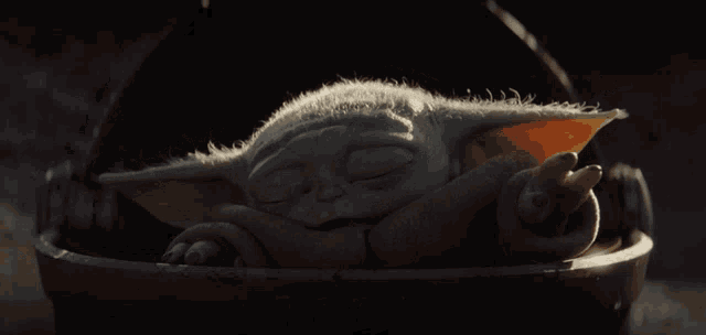 a baby yoda is sleeping in a bucket with his eyes closed