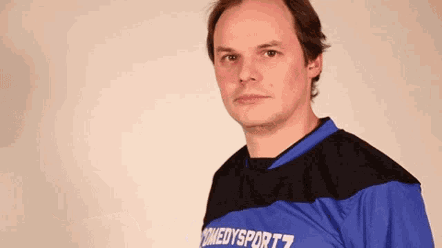 a man wearing a blue shirt that says comedysportz looks at the camera