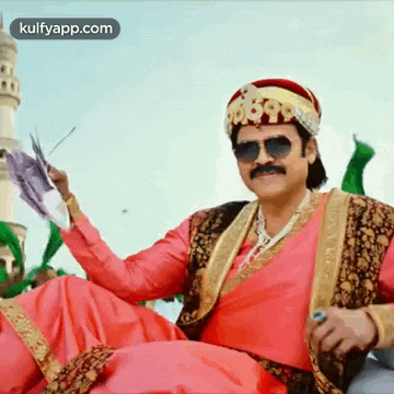 a man in a costume is holding a fan and wearing sunglasses and a turban .