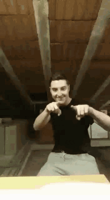 a man in a black shirt and grey sweatpants is pointing at the camera while dancing in a room .