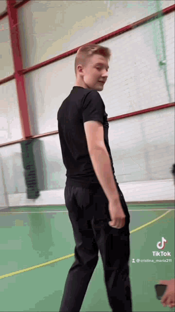a young man wearing a black shirt and black pants is standing on a green court .