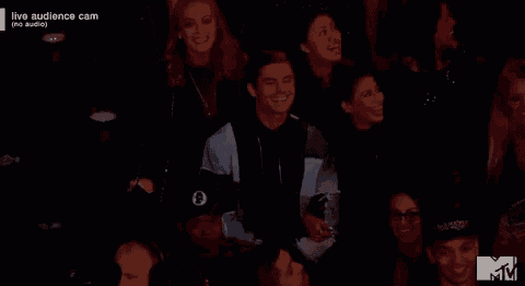 a group of people are sitting in a dark room watching a live audience cam