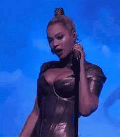 a woman is singing into a microphone on a stage in front of a blue sky .