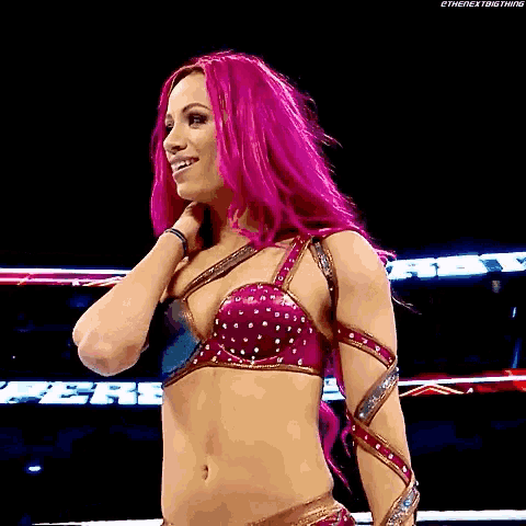 a woman with pink hair is standing in a wrestling ring smiling .