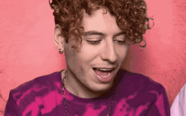 a man with curly hair is wearing a purple tie dye shirt and necklace