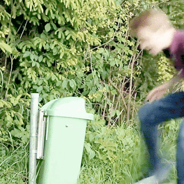 a person standing next to a green trash can with a purple shirt on