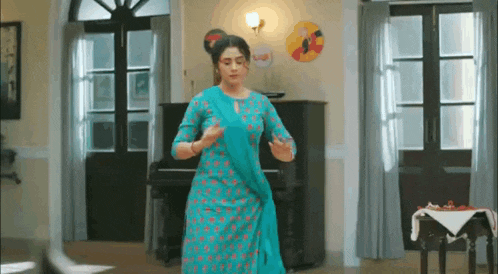 a woman in a blue dress is dancing in a living room with a piano .