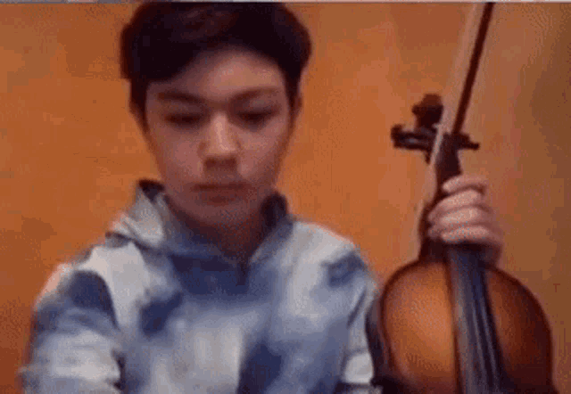 a young boy is playing a violin in front of a brown wall