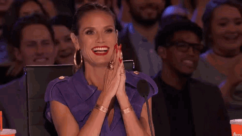 a woman in a purple dress is clapping her hands in front of a microphone in a crowd .