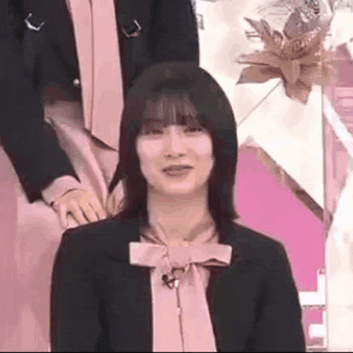 a woman in a pink shirt and black jacket is sitting in front of a microphone .