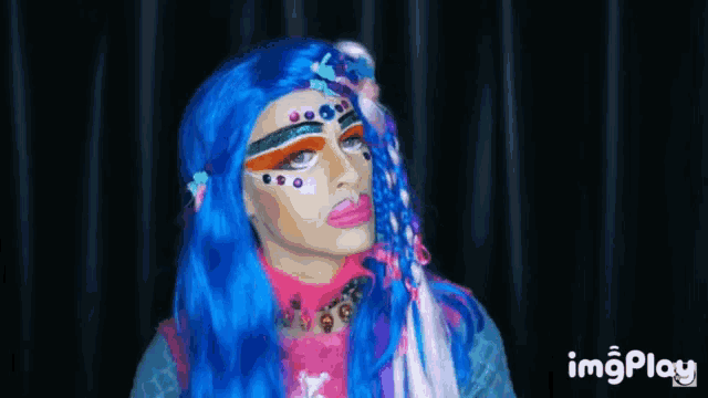 a woman with blue hair and makeup is wearing a blue wig and a pink shirt .